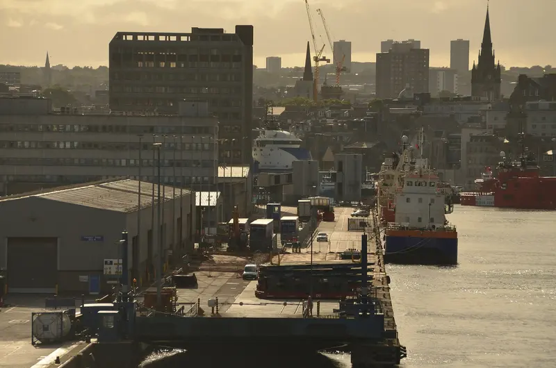 Supply ships moored in Aberdeen harbour in evening light, with the city's rooftops and church spires behind