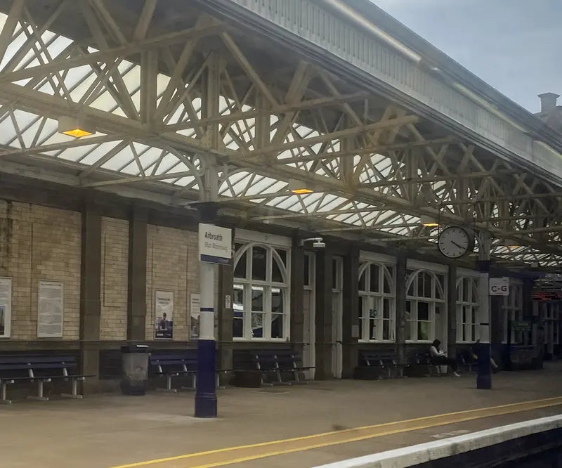 Arbroath station platform under a glazed canopy on lattice steel trusses, with the station clock and sash-windowed building