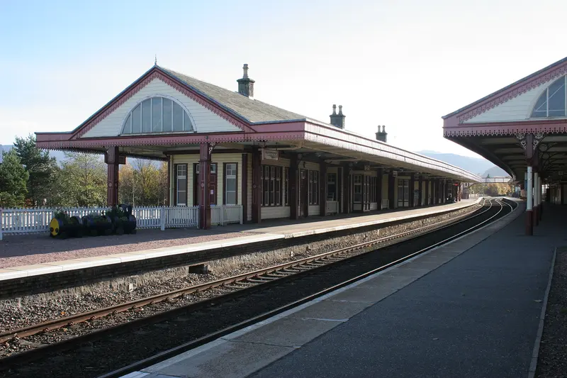 Aviemore station's timber platform buildings with pink-trimmed canopies and a large fanlight gable, curving away along the platform