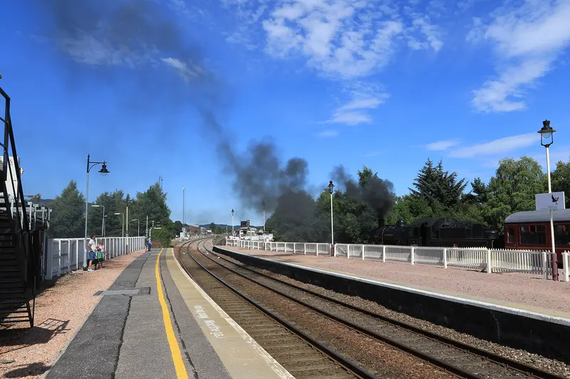 A steam locomotive leaving Aviemore with a plume of dark smoke under a blue sky