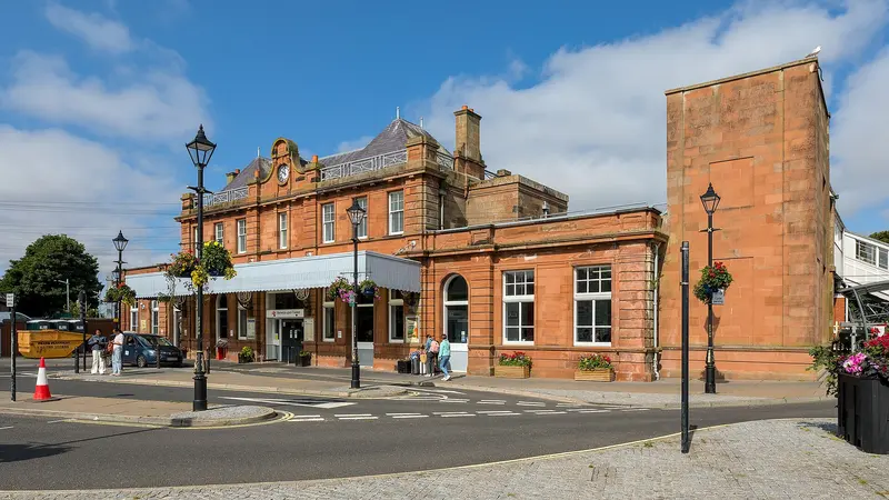 Berwick-upon-Tweed station's red sandstone building with its clock gable, glazed canopy and hanging flower baskets under a blue sky