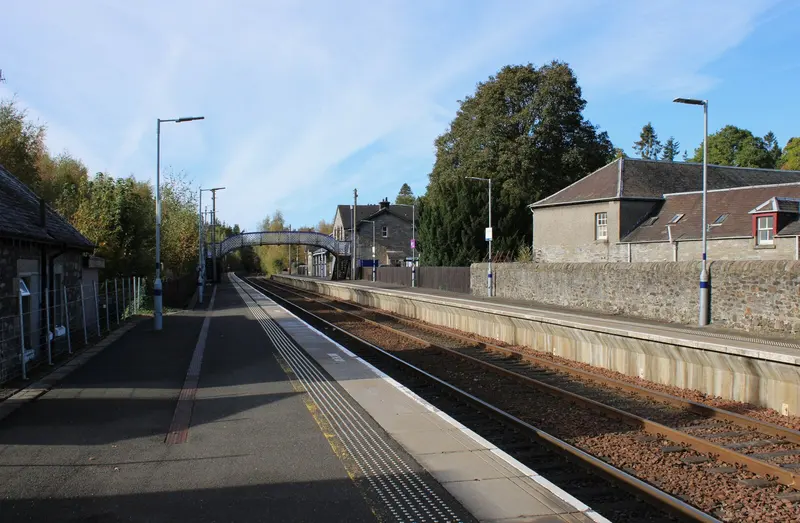 The platforms at Blair Atholl on a sunny day, with the stone station buildings and footbridge