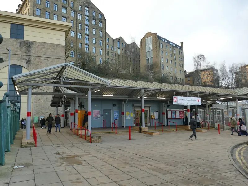 The low canopied entrance to Bradford Forster Square station, with older stone buildings rising behind