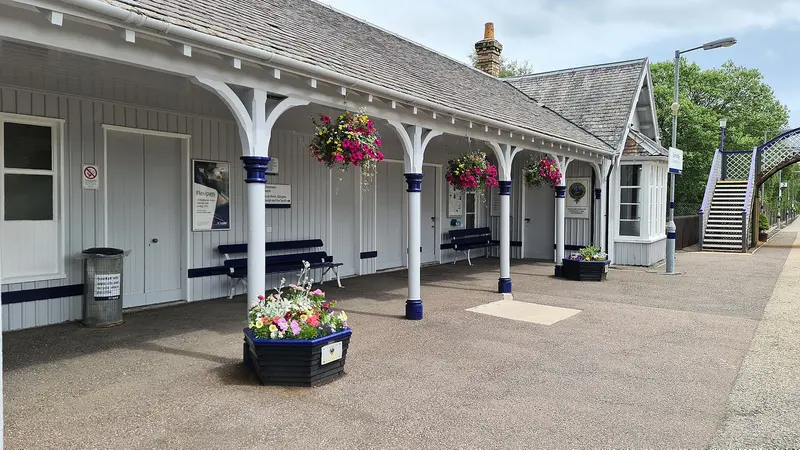 The platform at Carrbridge under a timber awning on cast-iron columns, with hanging baskets and flower tubs