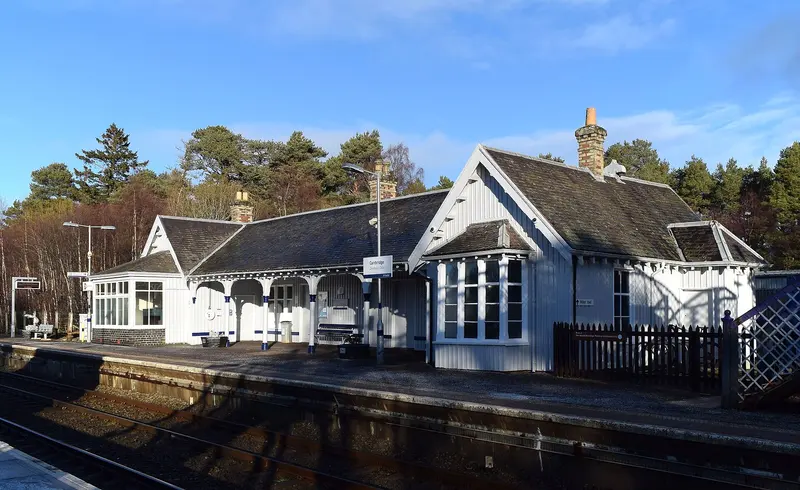 Carrbridge's white timber station building with gables, bay windows and a tall brick chimney beside the platform