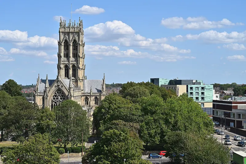 The tall Gothic tower of Doncaster Minster rising above trees and city-centre buildings under a blue sky