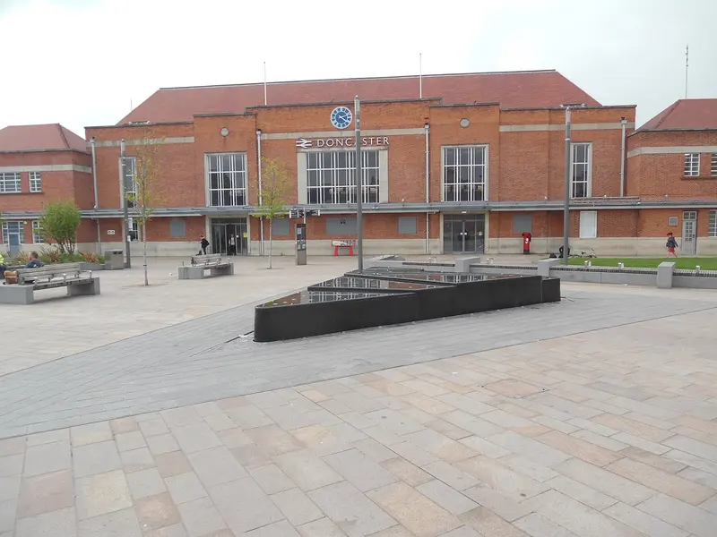 The red-brick 1930s frontage of Doncaster station with a central clock, seen across a paved square