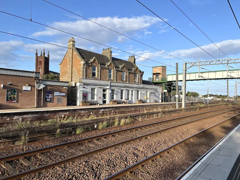 Dunbar's Tudor-style stone station building and platform 1 seen across the tracks from platform 2, with the footbridge and a church tower behind