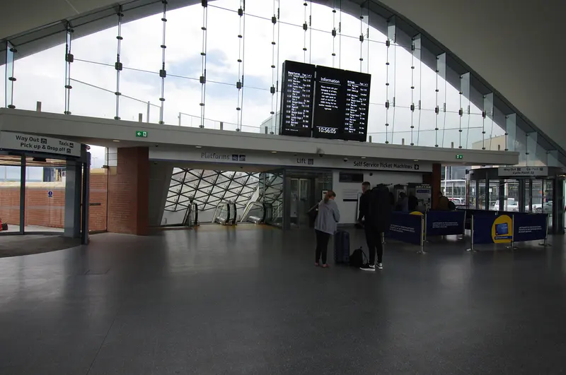 Dundee station's spacious concourse with a tall glazed wall, a departures board and the ticket gates