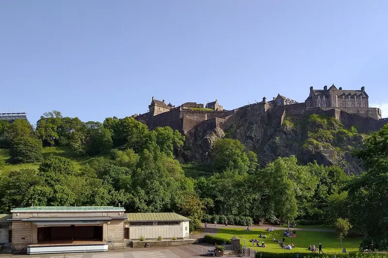 Edinburgh Castle on its volcanic rock above the trees of Princes Street Gardens under a clear blue sky