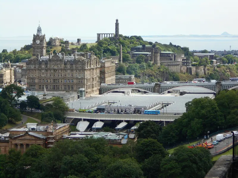 View east from Edinburgh Castle over the station roofs to the Balmoral Hotel clock tower and Calton Hill, with the Firth of Forth beyond