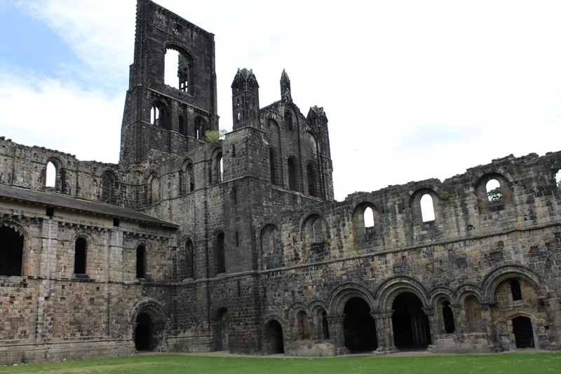 Roofless stone walls and tower of Kirkstall Abbey above a lawn
