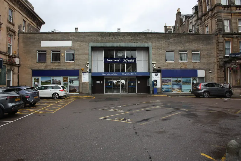 The main entrance of Inverness station, a low stone-clad building with a clock above the glazed doors