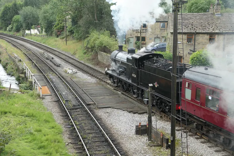 A black steam locomotive pulling maroon carriages away from Haworth on the Keighley and Worth Valley Railway, with steam billowing