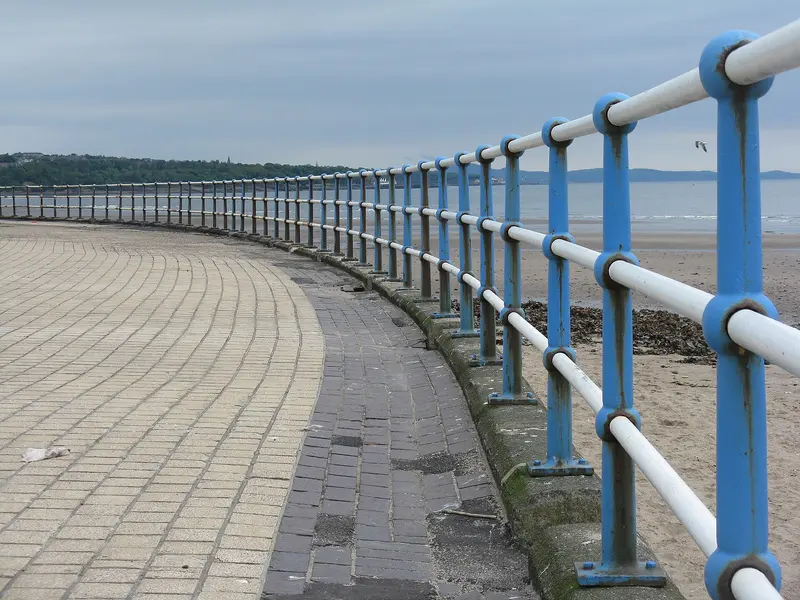 Kirkcaldy's curving seafront promenade with blue railings above a sandy beach on the Firth of Forth