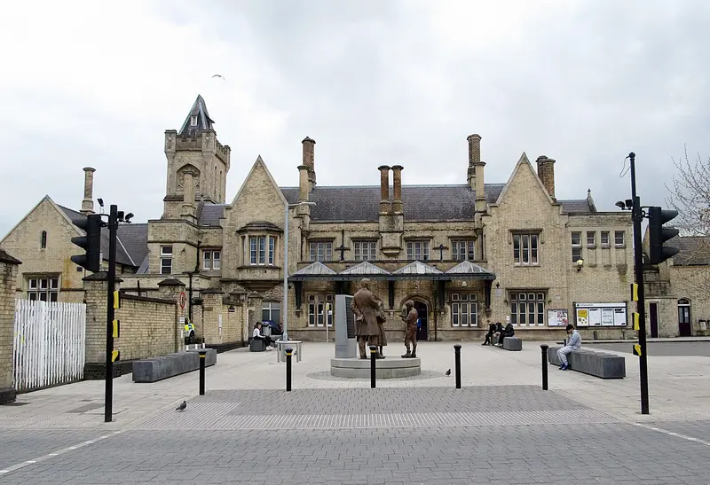 The Tudor-style stone front of Lincoln station, with its clock tower and tall chimneys, facing a pedestrian plaza