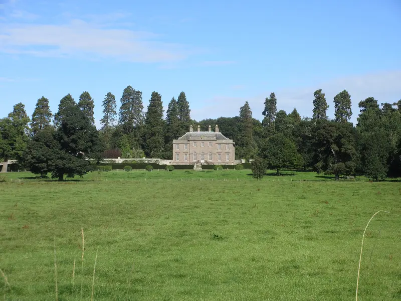 The pale stone Georgian mansion of House of Dun seen across a green parkland field, framed by tall trees