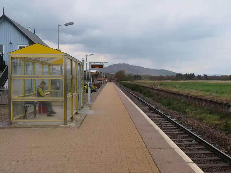 Newtonmore's single platform with a glazed waiting shelter and hills on the horizon