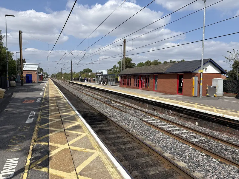 Northallerton station's two platforms and waiting room under overhead wires on a sunny day