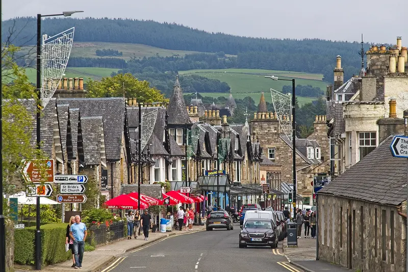 Pitlochry's main street lined with Victorian stone buildings, with green hills rising behind the town
