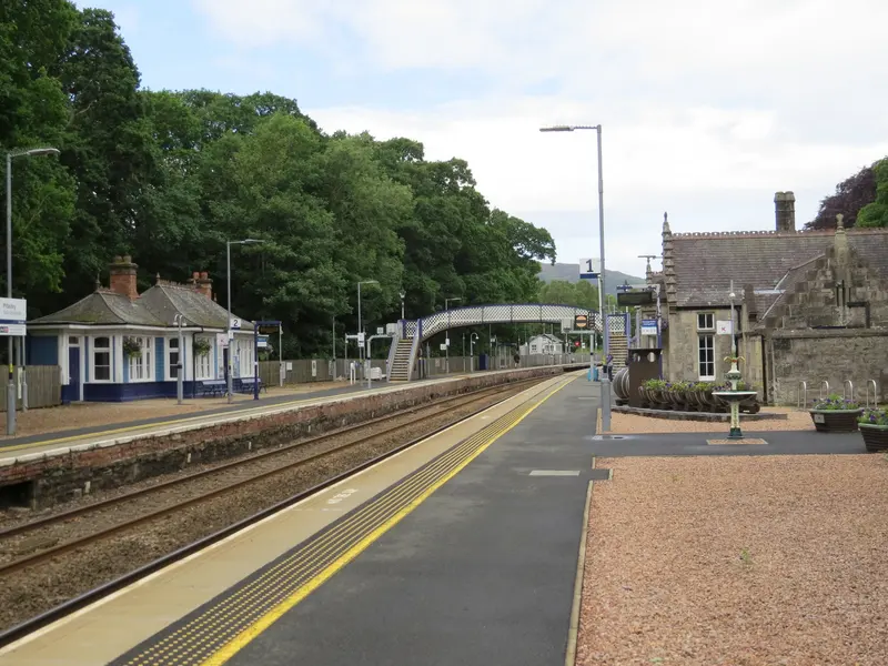 Looking along the platforms at Pitlochry, with a lattice footbridge, a wooden waiting room and wooded hills behind