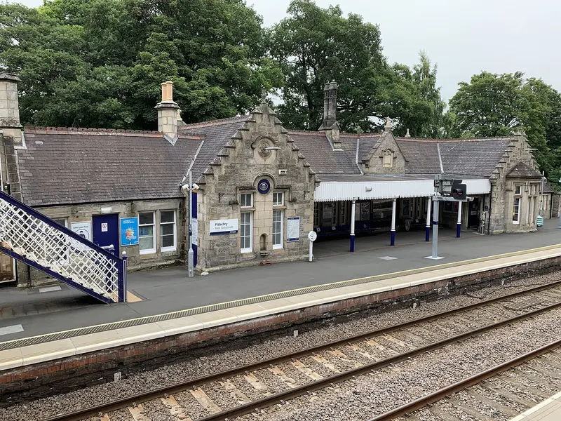 Pitlochry's stone station building with crowstepped gables and a canopy over the platform