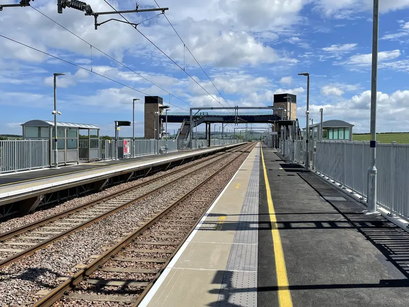 The two long platforms at Reston station under a blue sky, with the footbridge and its lift towers in the distance