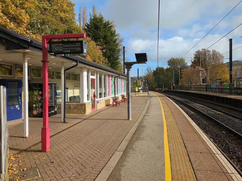Platform 1 at Shipley station in autumn, with a red-framed canopy, waiting room and trees beyond the tracks