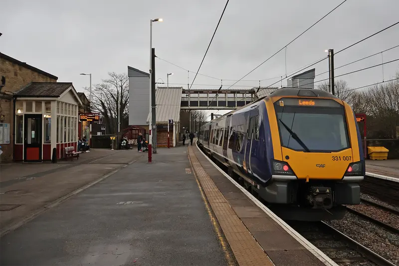 A Northern electric train at a platform at Shipley, with the station's stone buildings and footbridge behind