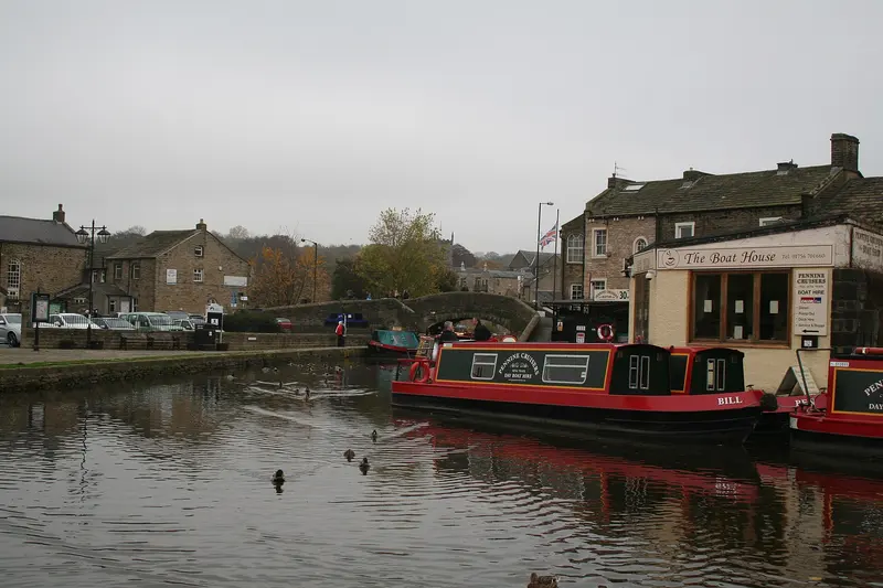 Red narrowboats moored on the Leeds and Liverpool Canal in Skipton, with stone buildings along the water